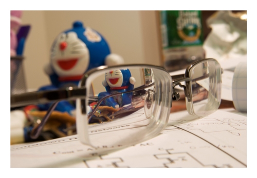 Close-up photograph of eyeglasses, homework, small stuffed animal.