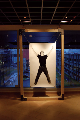 Full body photograph of a person, displayed in a wooden frame against a blue outside background.