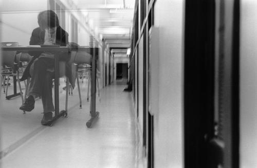 Photograph of hallway, reflections off glass, a student at a desk.