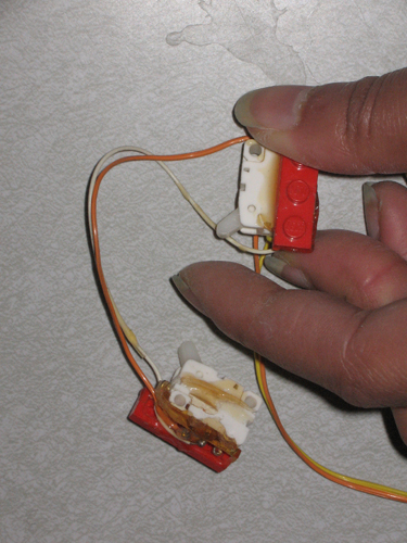 These push sensors are epoxied to LEGOs for easy mounting, and have a switch protruding from one corner. Wires connect the sensors in series.