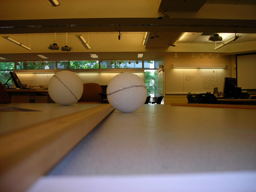Two styrofoam balls on a table are photographed at eye level making them appear much larger than their actual size.
