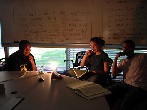 Three students sit at a table with a lit lightbulb and a radiometer.