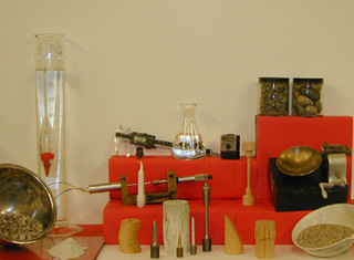 A photo of various equipment- like a caliper, scale, beaker with sample materials like pieces of wood, metal and stone.