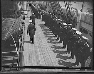 A black and white photo of two officers inspecting sailors on deck.