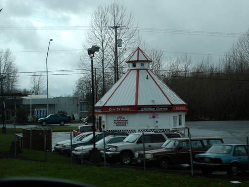 A white and red striped hut in a parking lot dispenses coffee to commuters.