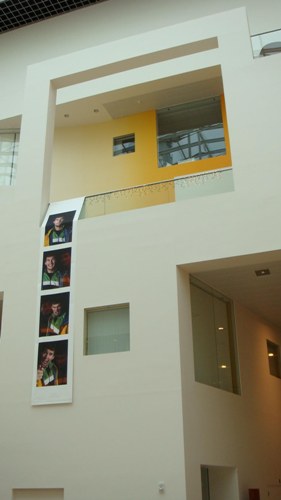 Four photographs displayed on a vertical strip, hanging from an upper floor of the building.
