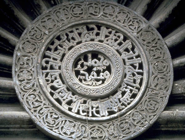The central medallion above the entrance door with a Qur'anic verse inscribed around the central ring, which contains the words 'Muhammad' and '`Ali'.