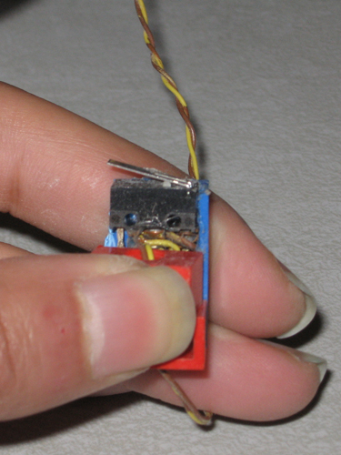 This sensor and metal arm are each ~1 cm long, and the white switch is barely visible near the fixed end of the arm.