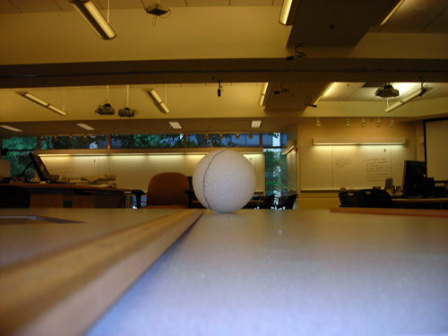 A styrofoam ball on a table is photographed at eye level making it appear much larger than its actual size.