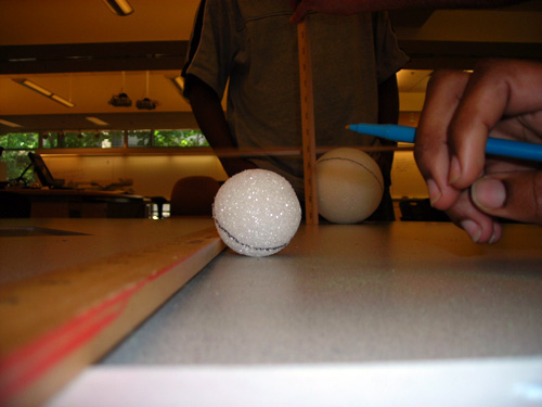 Two styrofoam balls on a table are measured with a ruler to determine their angular size.