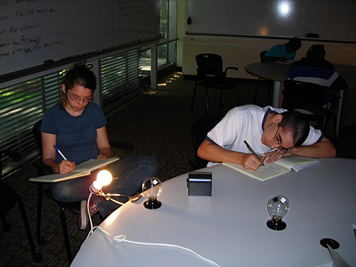 Three students sit at a table with a lit lightbulb and a radiometer.