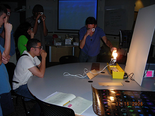 Students hold slides up to their eyes looking at a lit lightbulb.