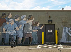 A photo of a mural depicting a group of people standing in front of a bulldozer. The bulldozer reads "Federal Inner Belt I-95".