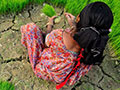 A woman sitting in an agricultural field with cracked, dry earth.