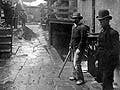 Men in bowler hats stand in the alleyway of a tenement house. Laundry hangs on lines above them. 