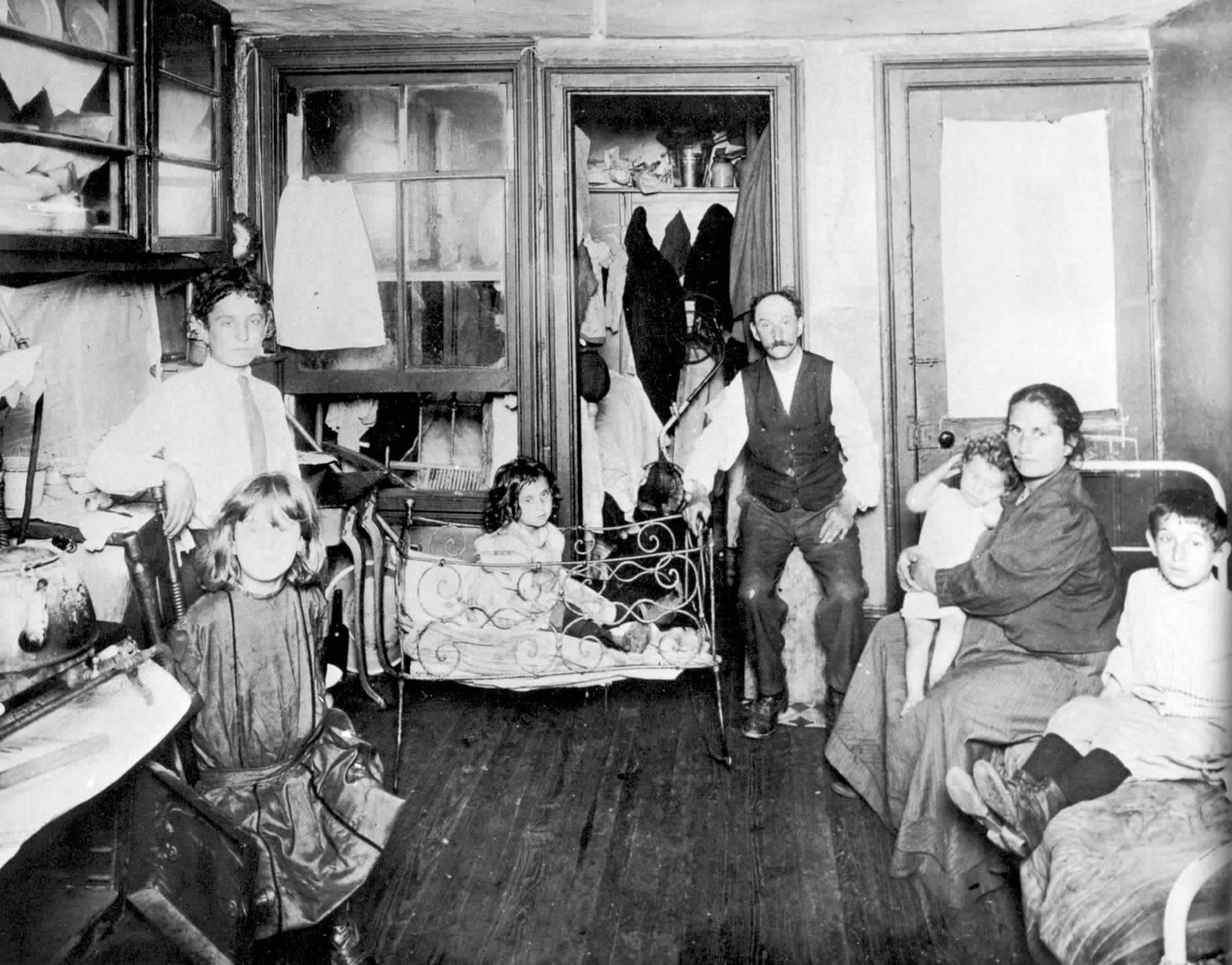 A black-and-white photo of a family of seven people in a cramped and shabby room.