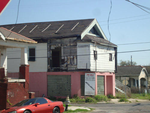 A dilapidated white and pink building sits on the corner in a neighborhood.