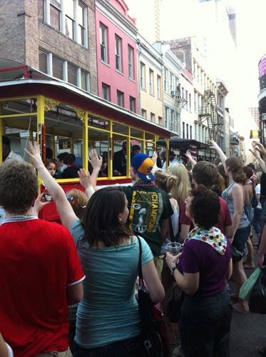 A trolley drives down a street crowded with people during a parade.