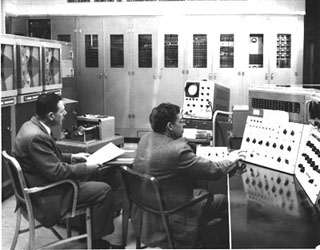 A photograph of two engineers sitting before a massive computer.
