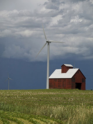 A wind turbine towers over a small red farmhouse.