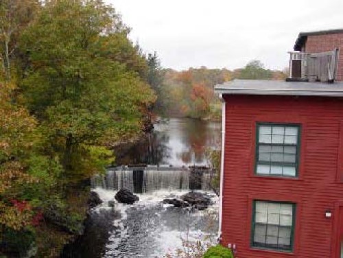 An old mill building by a dam on a river, with autumn trees on the banks