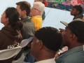 An African-American woman smiles and gestures as she addresses a diverse group of listeners.