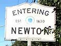 A photograph of cars on a street next to a sign that says "Entering Newton."