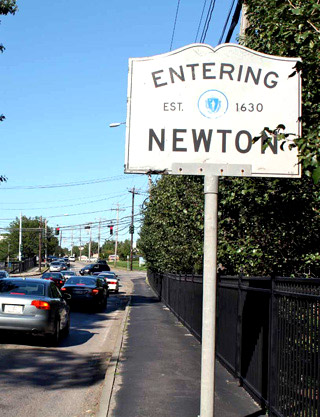 A photograph of cars on a street next to a sign that says "Entering Newton."