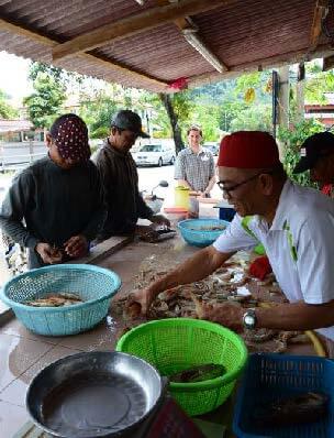 A  man in a white shirt and a red hat sorts through fish and shrimp on a counter. A few men stand around him.