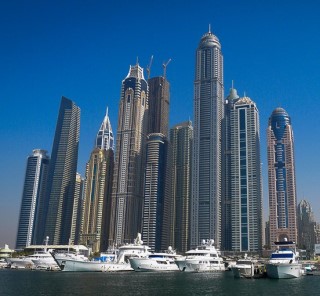 A cluster of modern skyscrapers, with yachts docked in a harbor at their feet