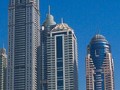 A cluster of modern skyscrapers, with yachts docked in a harbor at their feet