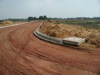 A photograph of a new road being constructed in Vietnam.  The photograph shows a recently graded dirt surface as well as curbs and and a drainage system.