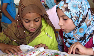 Two girls in headscarves read together from a book.