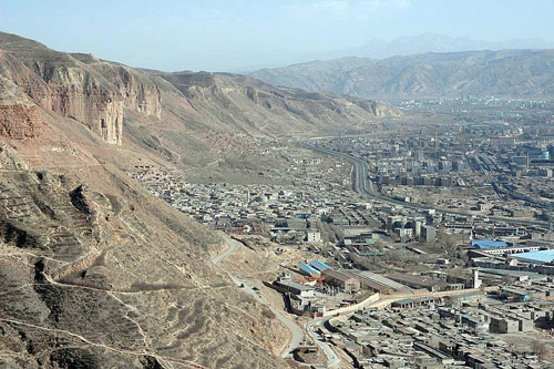 A built up town in an arid valley surrounded by mountains.