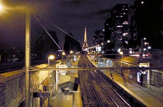 A photo of the Paris Metro tracks heading off to a lit Eiffel Tower on the horizon.