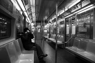Black and white photograph of one rider on a mostly empty subway.