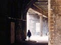 An opening to a dark arched passage leading to a sunlit space, with a silhouetted human figure.