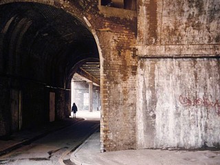 An opening to a dark arched passage leading to a sunlit space, with a silhouetted human figure.