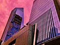Two glass buildings rise into the sky. They glow pink as they reflect the sunset. 