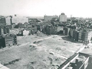 A bird's-eye view of an urban renewal project, with a large barren area abutting a densely-built block of tenements.