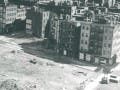A bird's-eye view of an urban renewal project, with a large barren area abutting a densely-built block of tenements.