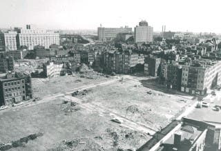 A bird's-eye view of an urban renewal project, with a large barren area abutting a densely-built block of tenements.