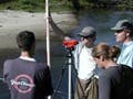 Four people with survey equipment near a river.