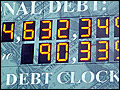 A photograph of a billboard sized electronic clock on a brick wall that displays the national debt of the United States.