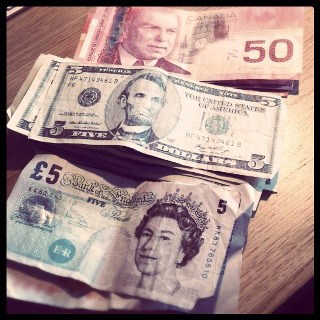 A photograph of stacks of Canadian fifty dollar, American five dollar, and British five pound notes lined up on a table.