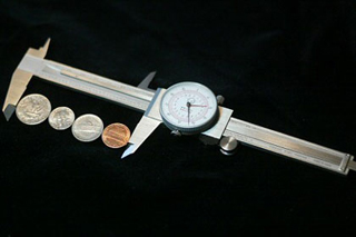 Photograph of four coins laid flat between the points of a caliper.