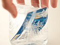 A hand holds a clear glass that contains a credit card frozen in ice. 