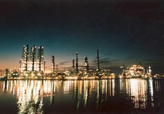 Photo of a refinery lit at night, reflected in water.