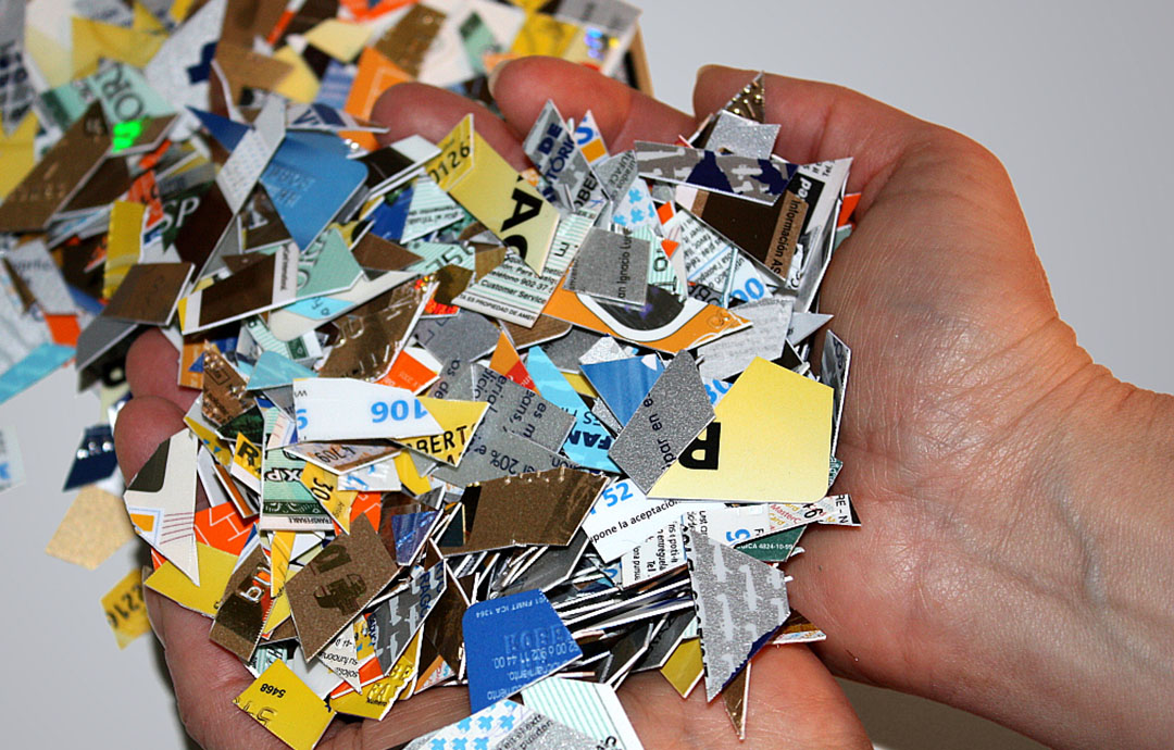 A person holds a pile of multi-colored fragments of plastic credit cards that have been up cut up. 
