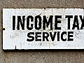 Photograph of a white sign with black print advertising income tax preparation.